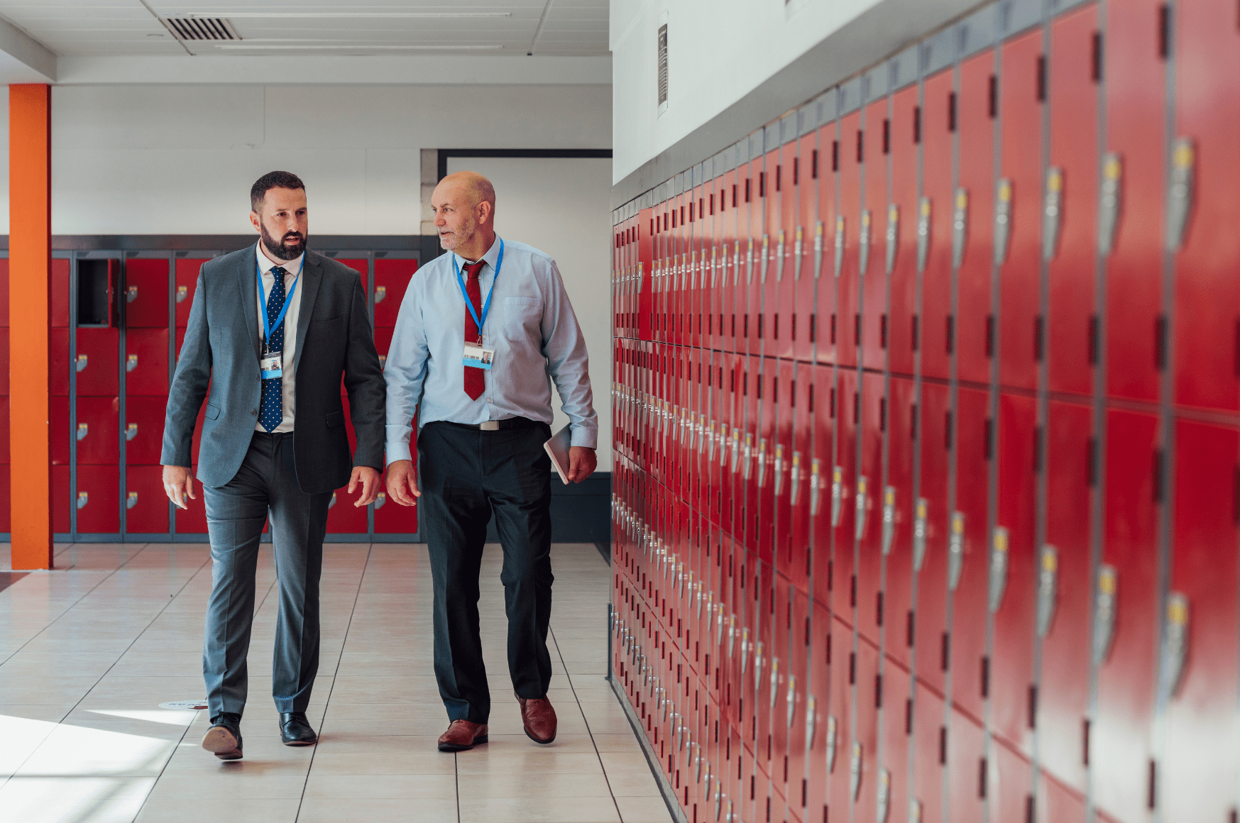 two men walking in school hallway next to red lockers