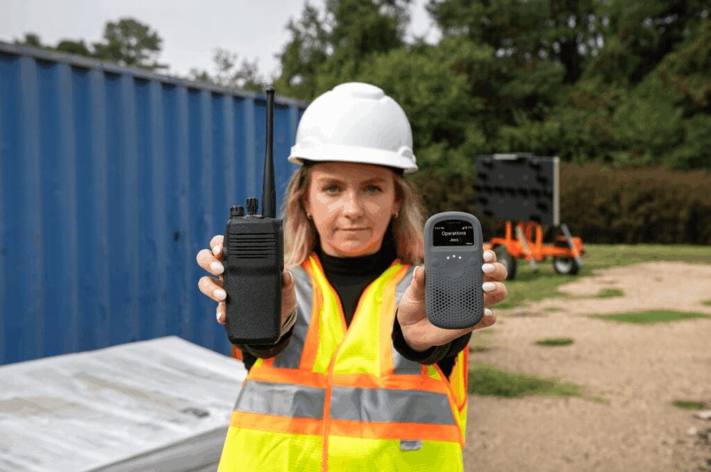 Woman on construction site holding RelayX and traditional walkie talkie