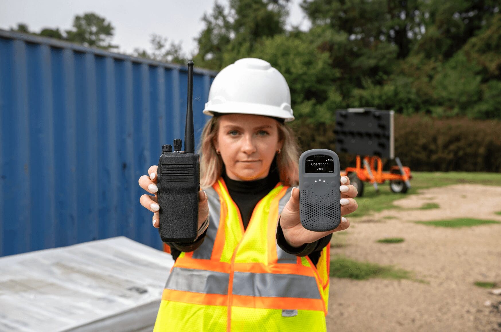 Woman on construction site holding RelayX and traditional walkie talkie