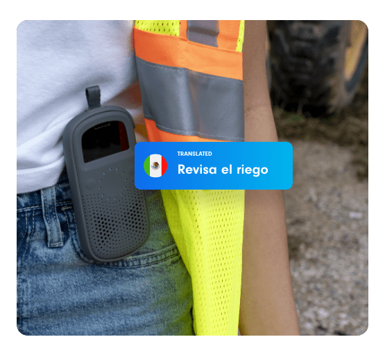 Close-up of a Relay device clipped to a farm worker's waist, displaying the translated message “Revisa el riego.”