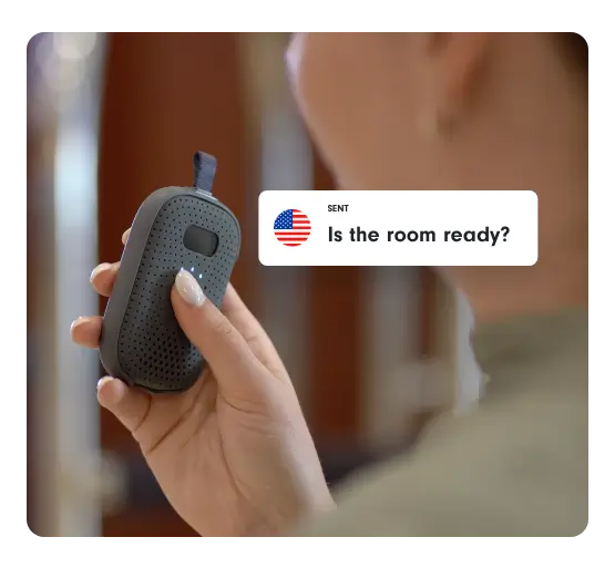 Hotel staff member speaks into RelayM device asking, “Is the room ready?” in English.