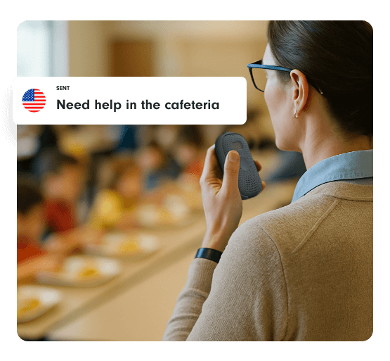 A teacher in a school cafeteria speaks into a Relay device, with a message bubble reading “Need help in the cafeteria.