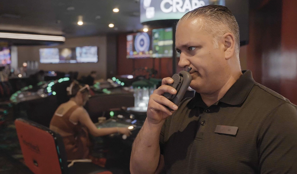 Casino staff member communicating with team using Relay device on a busy gaming floor.