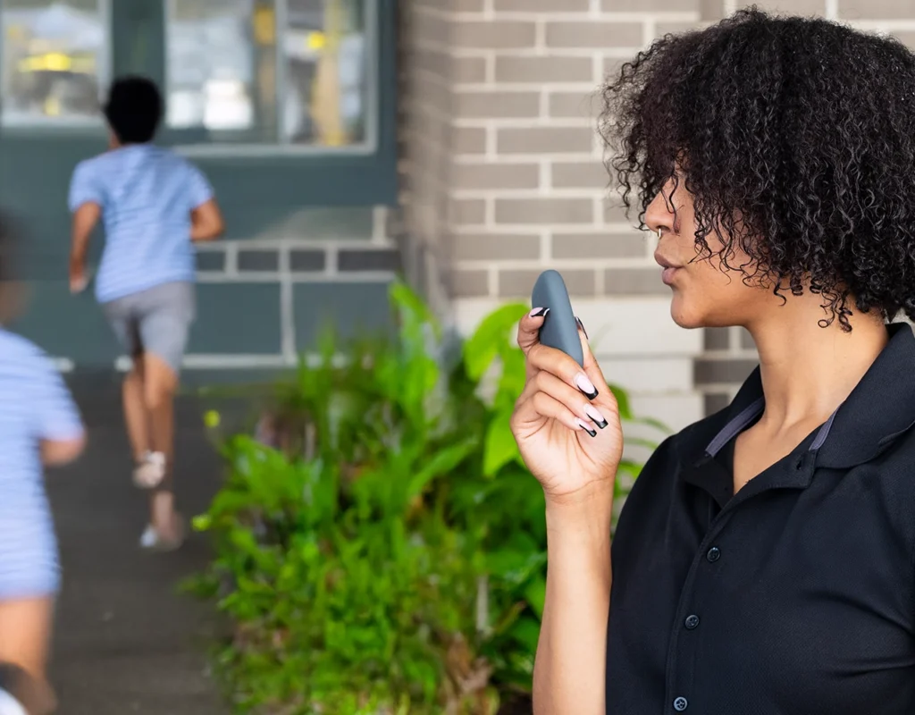 School staff member uses a Relay device for communication while supervising students outdoors.