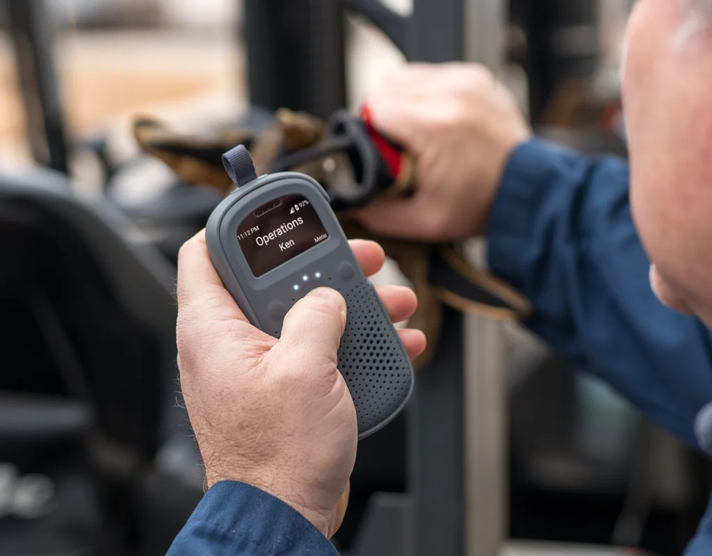 Close-up of a worker holding a Relay device with the screen showing “Operations” and the user “Ken.”