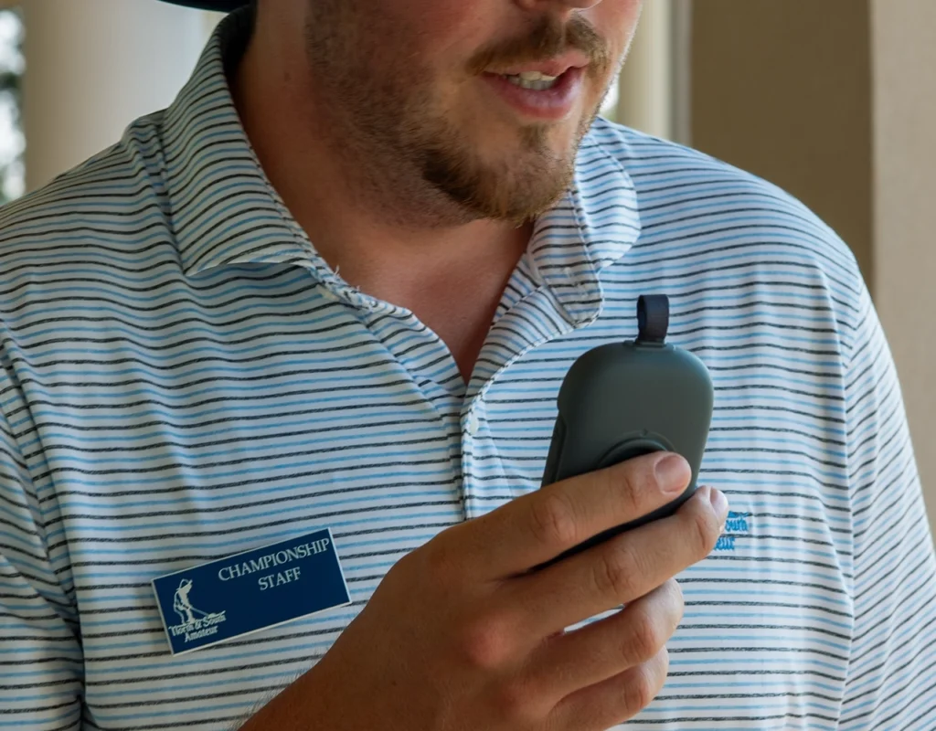 Pinehurst staff member speaking into a Relay device while wearing a striped polo and staff badge.