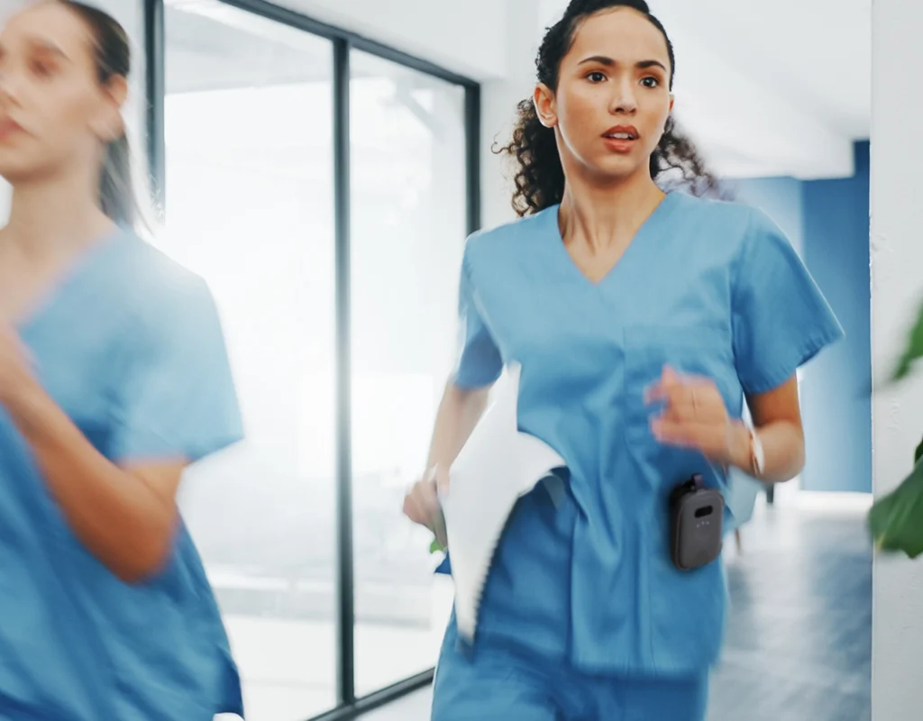 Nurse in blue scrubs running down a hospital hallway with a RelayM device clipped to her pocket for fast communication.