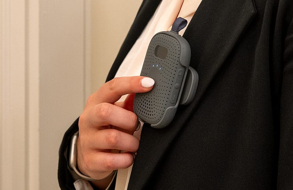 Person holding a gray RelayM device, pressing the button to send a panic alert.