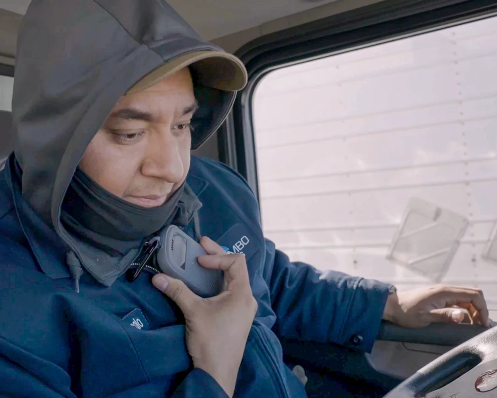 Delivery driver wearing a hooded jacket uses a RelayX device inside a truck cab to communicate with their team.