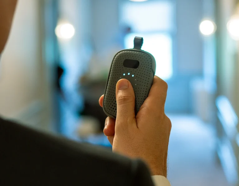 Hotel staff member holds a RelayM device in a hallway, pressing the button to send a panic alert.
