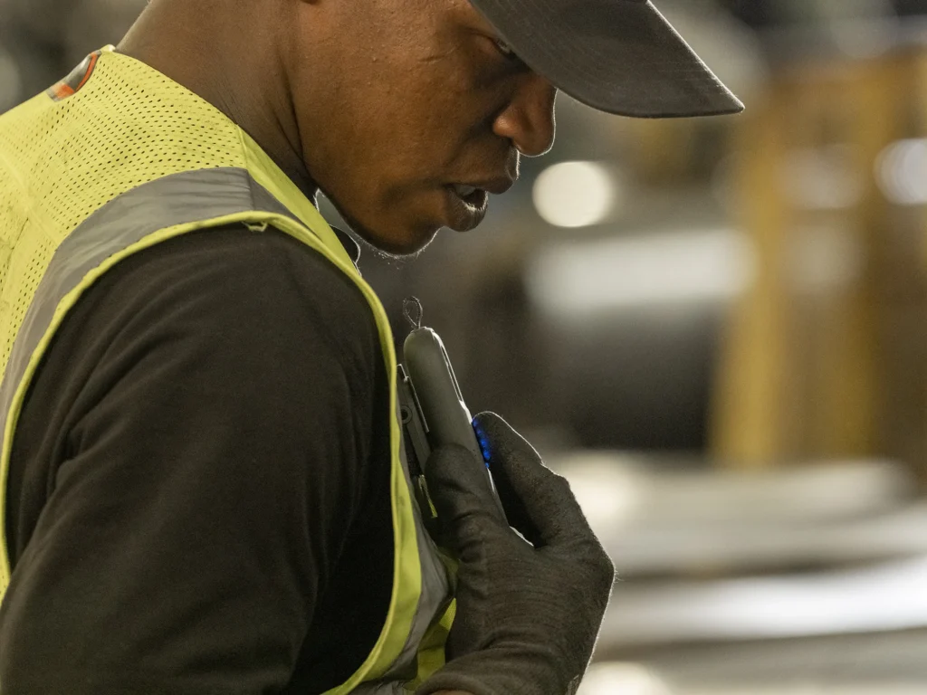 Worker in vest pressing to talk while wearing Relay device on their shoulder