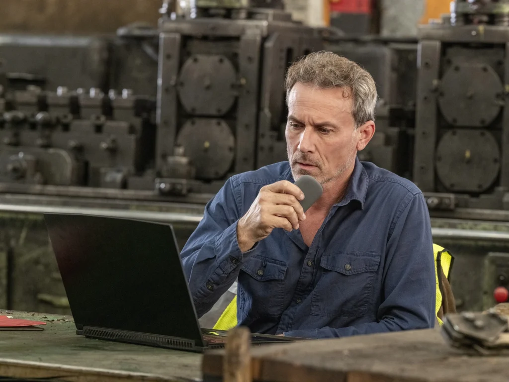 Plant operator at a workstation using a computer in an industrial setting and speaking into a Relay