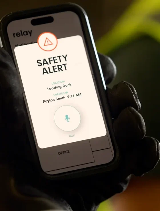 Worker holding a smartphone displaying a Relay safety alert for the loading dock.