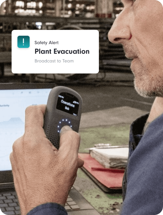 Factory supervisor uses a Relay device labeled "Operations – Bob" while sitting at a workstation with a laptop and clipboard in view.